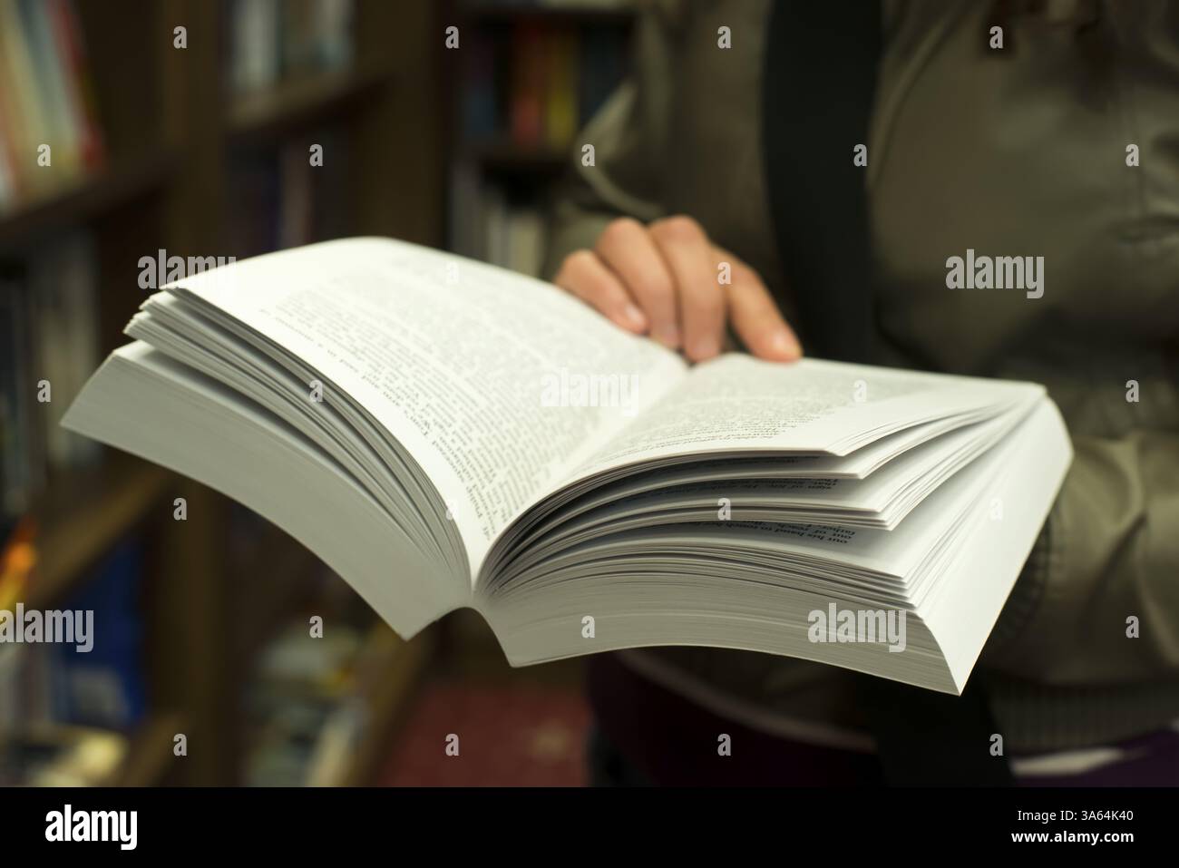 Hand holding open book in a bookstore. Many books on the background Stock Photo