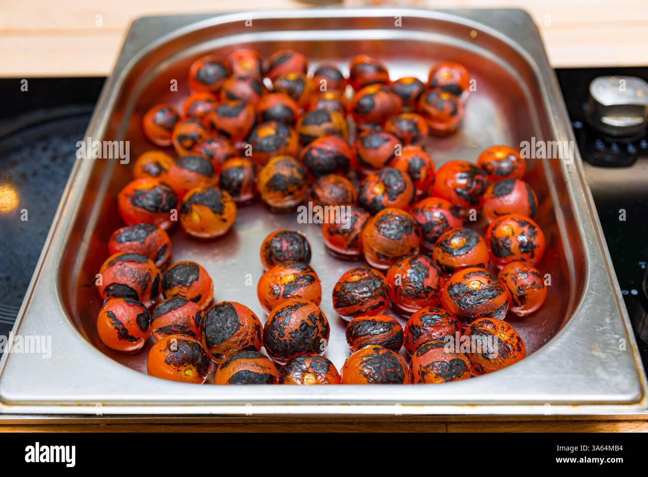 Fresh cherry tomatoes roasted to perfection with a charred skin, placed in a stainless steel tray, ready for cooking or serving. Stock Photo