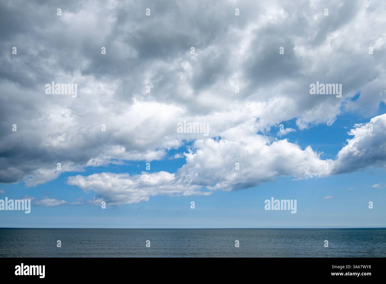 Blue sky with dramatic clouds dominates the scene, while the sea meets the distant horizon below. Stock Photo