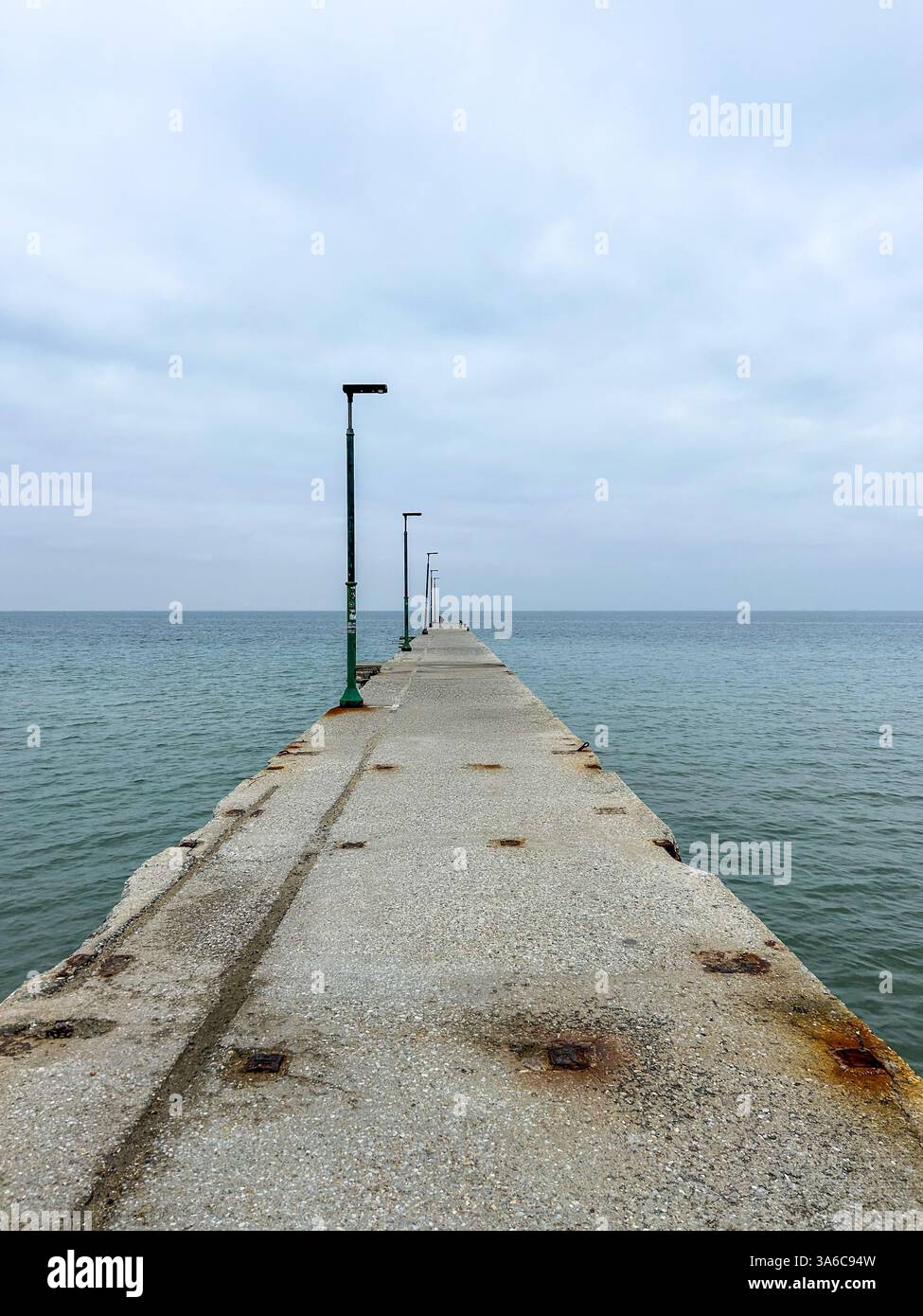 A quiet pier stretches into the sea under a moody, overcast sky in Agia Triada, capturing the calm and reflective atmosphere of a cloudy coastal day. - Smartphone Captured Stock Image