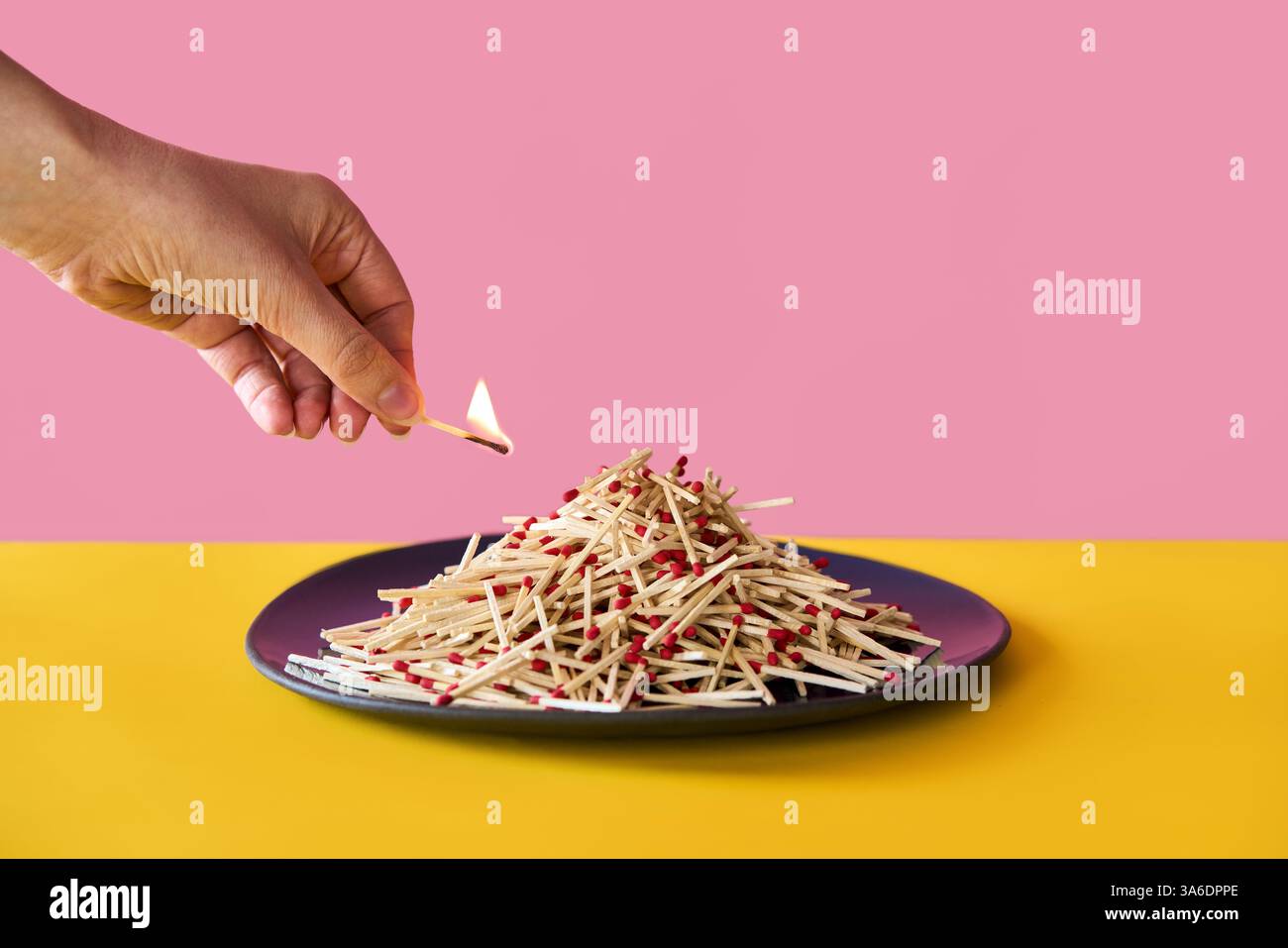 Hand holds burning matchstick above a large pile of matches on plate ...