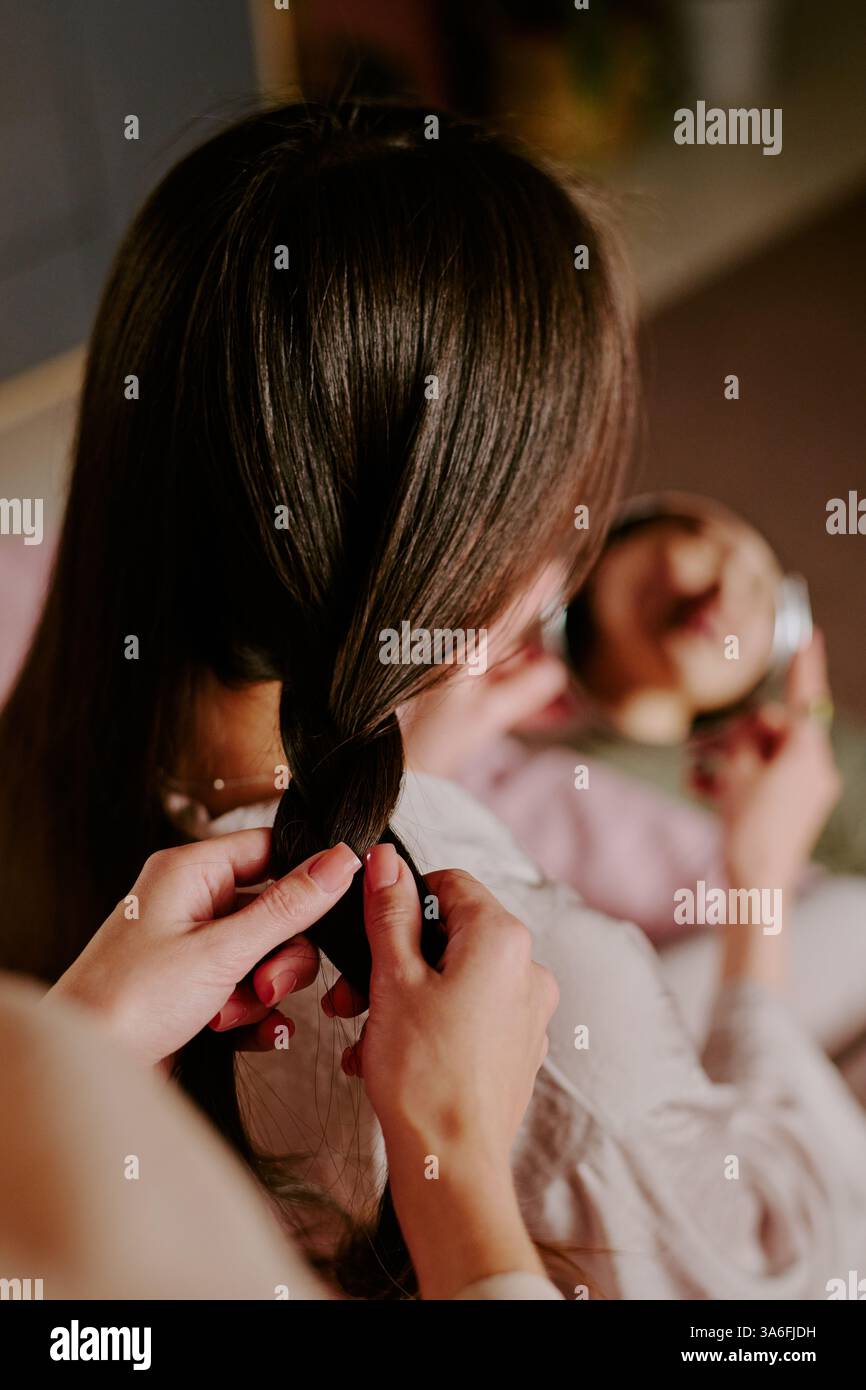 Vertical high angle shot of unrecognizable manicured hands braiding hair of woman Stock Photo