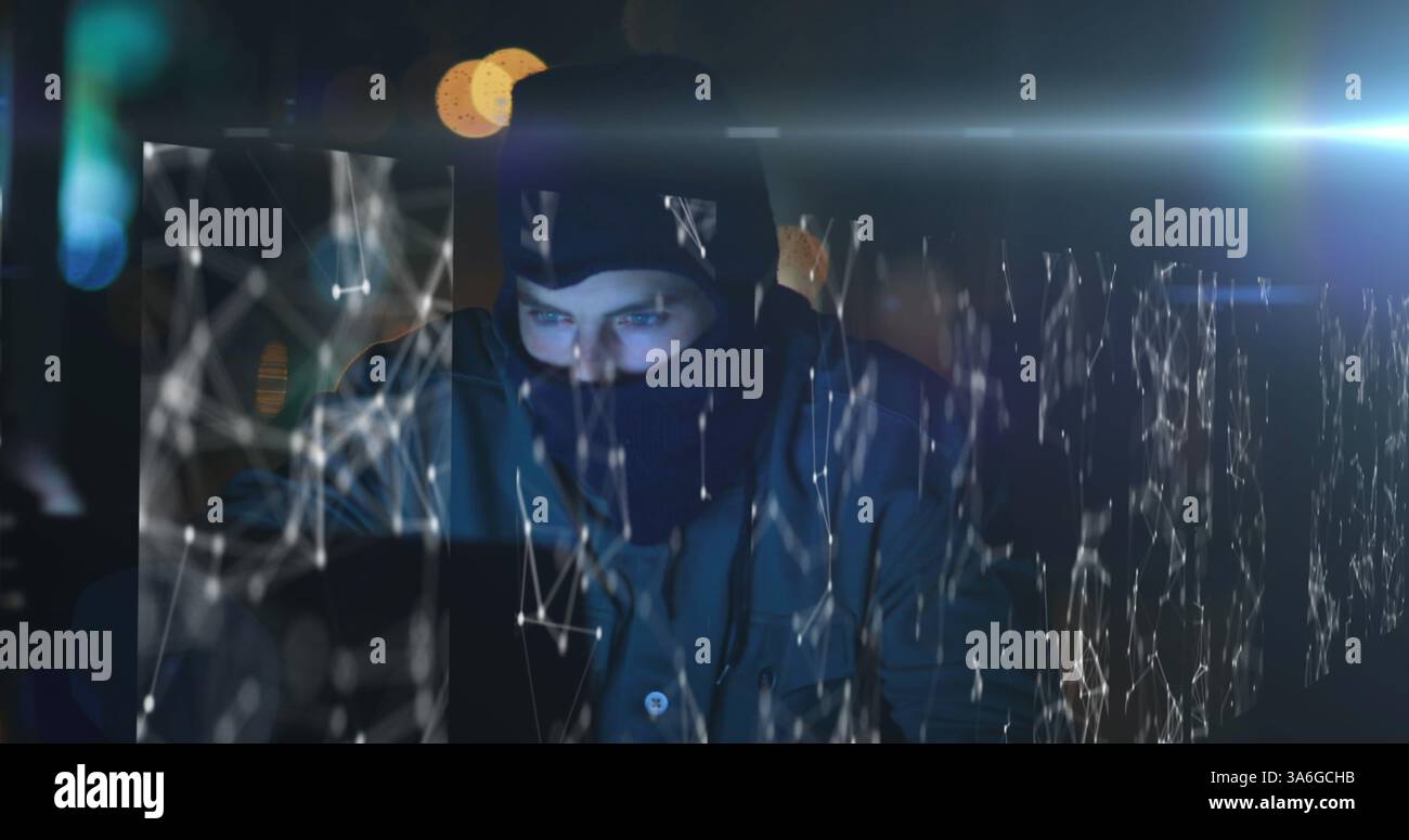 Hacker in dark room using laptop with digital network overlay, focused on screen. Cybersecurity, hacking, technology, espionage, coding, data Stock Photo