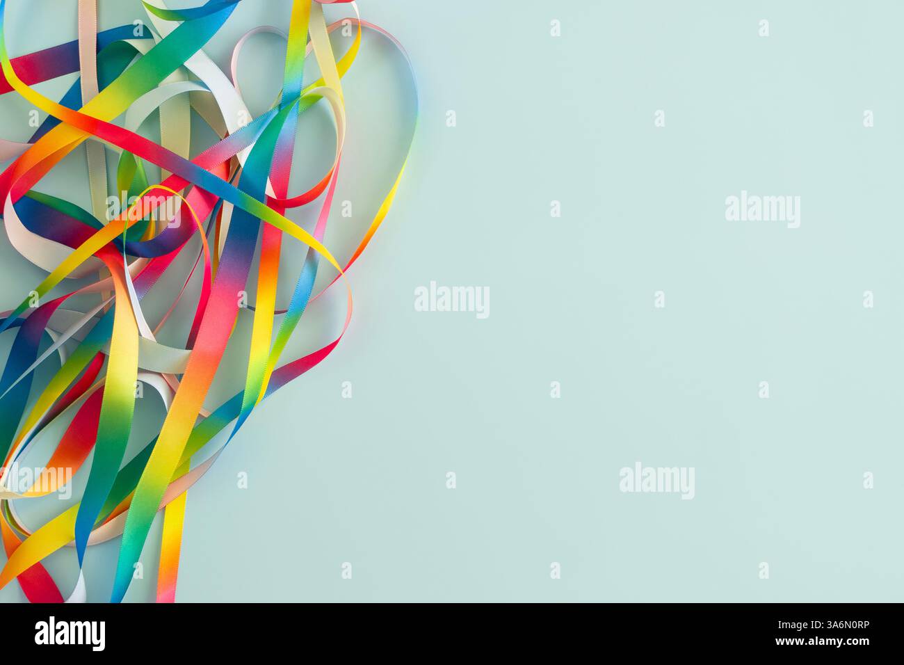Abstract frame with multiple rainbow satin ribbons scattered in irregular pattern, gently twisted, curling and looping on light blue background. Top Stock Photo