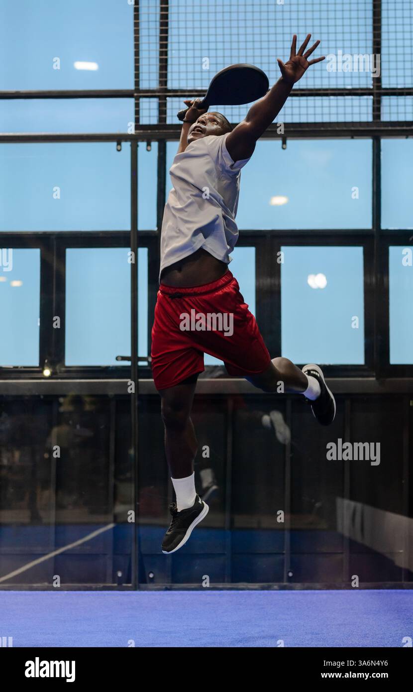 African American man jumping to hit ball during padel tennis match indoors Stock Photo