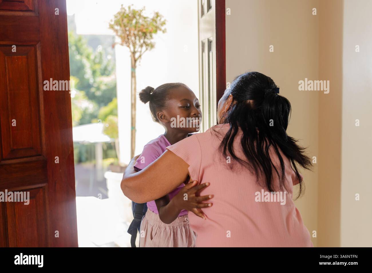 Grandmother hugging granddaughter at home entrance, sharing joyful welcome moment Stock Photo