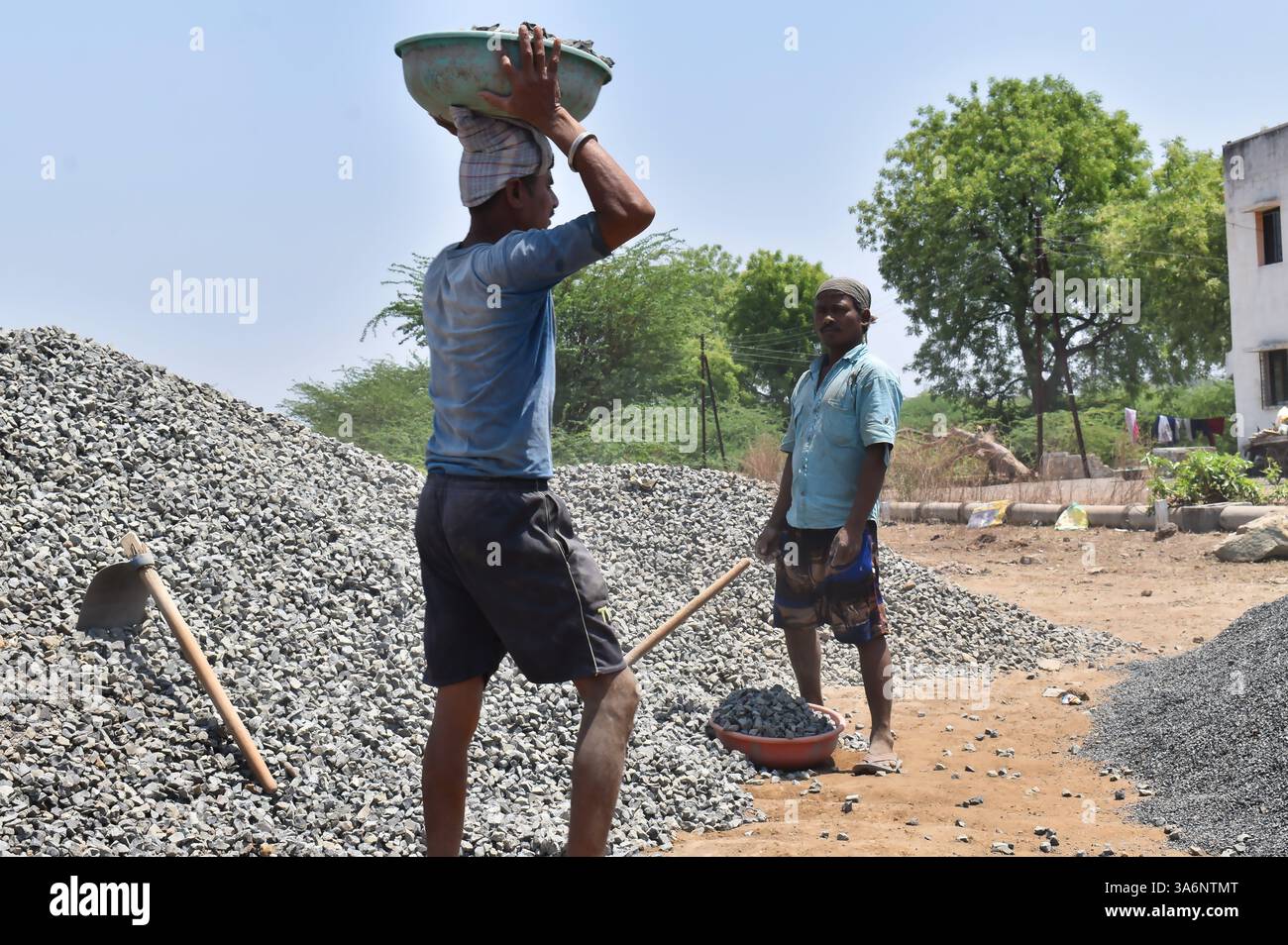 Two men working at a construction site, one carrying a basket of gravel ...