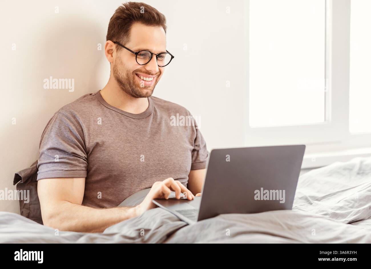 Man Using Laptop Browsing Internet Sitting In Bed At Home Stock Photo