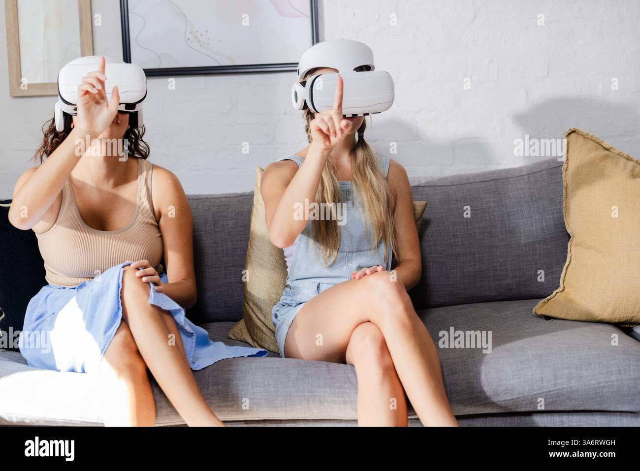 Women using VR headsets on sofa, exploring virtual reality together Stock Photo
