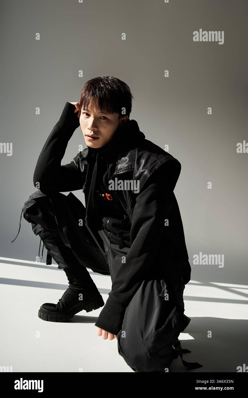 Stylish Asian man crouches in a modern studio, showcasing charisma and ...