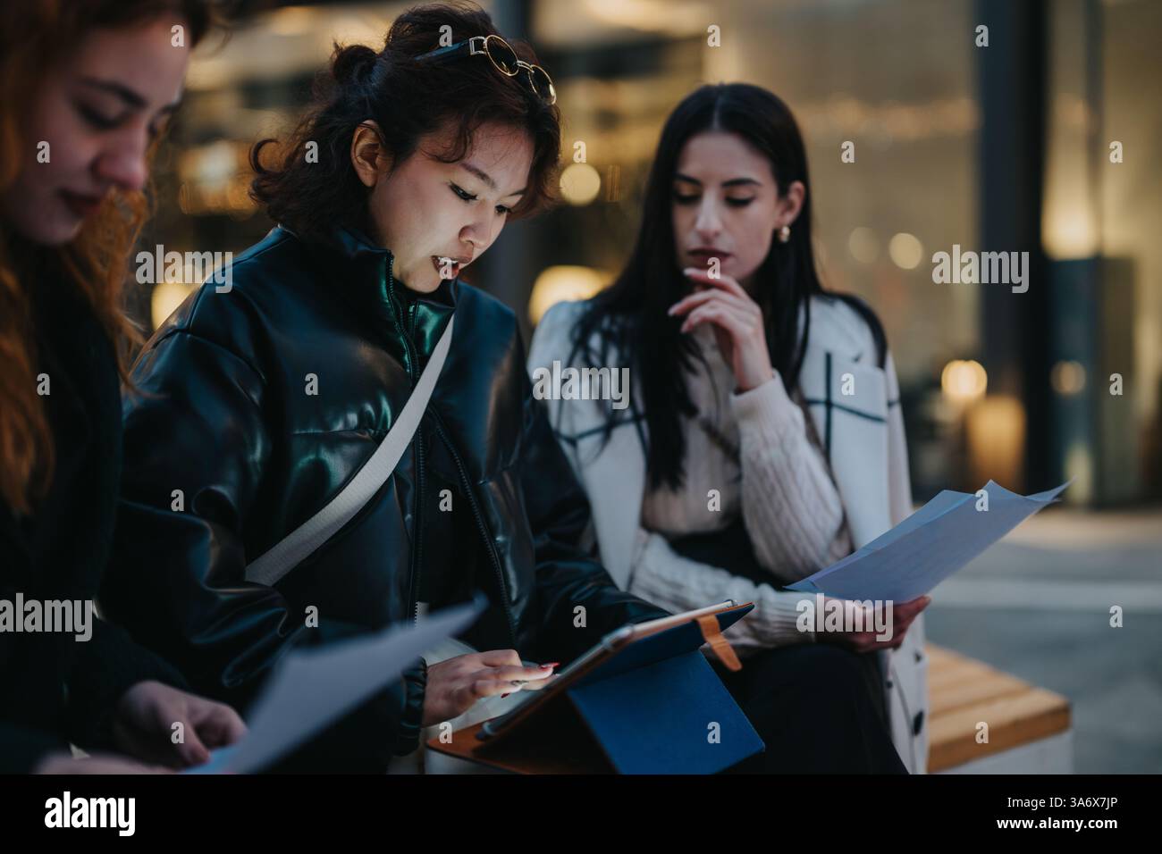 Young women collaborating outdoors, reviewing documents and using a digital tablet Stock Photo