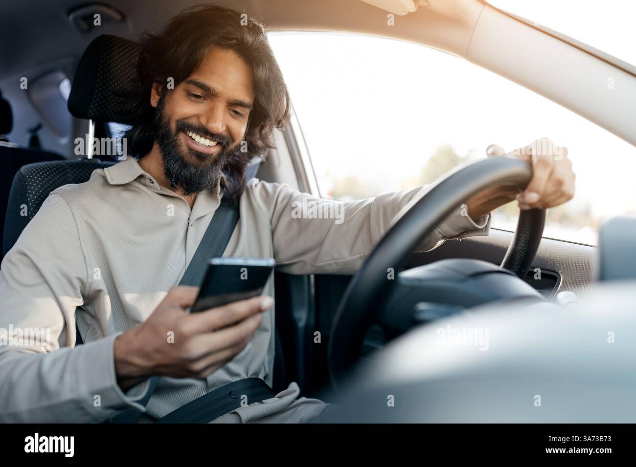 Unsafe driving. Cheerful indian man using smartphone while driving car Stock Photo