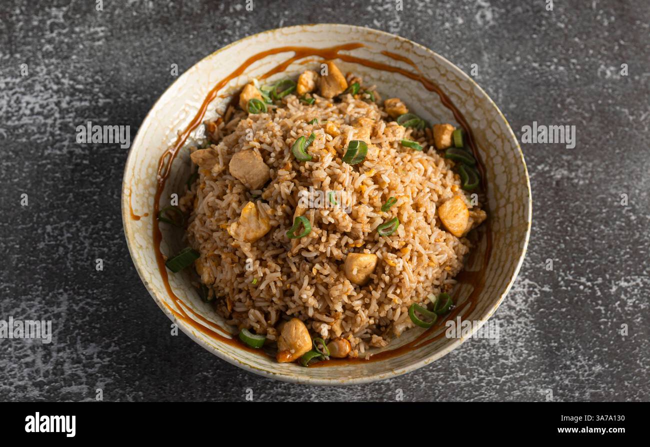 Steaming chicken fried rice seasoned with soy sauce and garnished with fresh green onions, served in a bowl Stock Photo