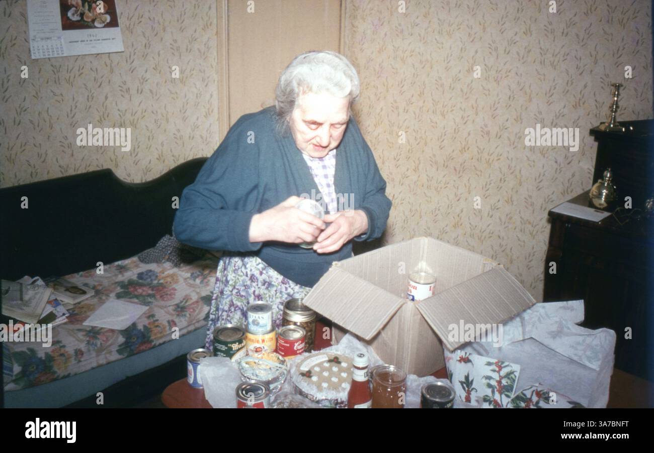 Photographed in 1962 on 35mm colour slide film, this image captures an elderly woman preparing a box of tinned food for a Christmas charity collection in her modestly decorated English home. A touching glimpse into post-war community spirit and festive generosity. Stock Photo