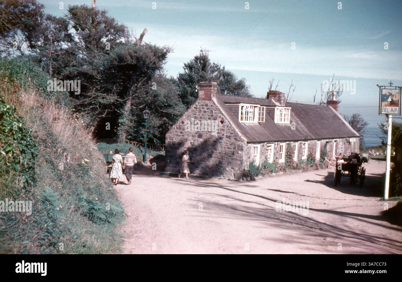 A tranquil 1960s scene on the Isle of Sark outside the Bel Air Pub, with visitors strolling along a dusty path. Stock Photo
