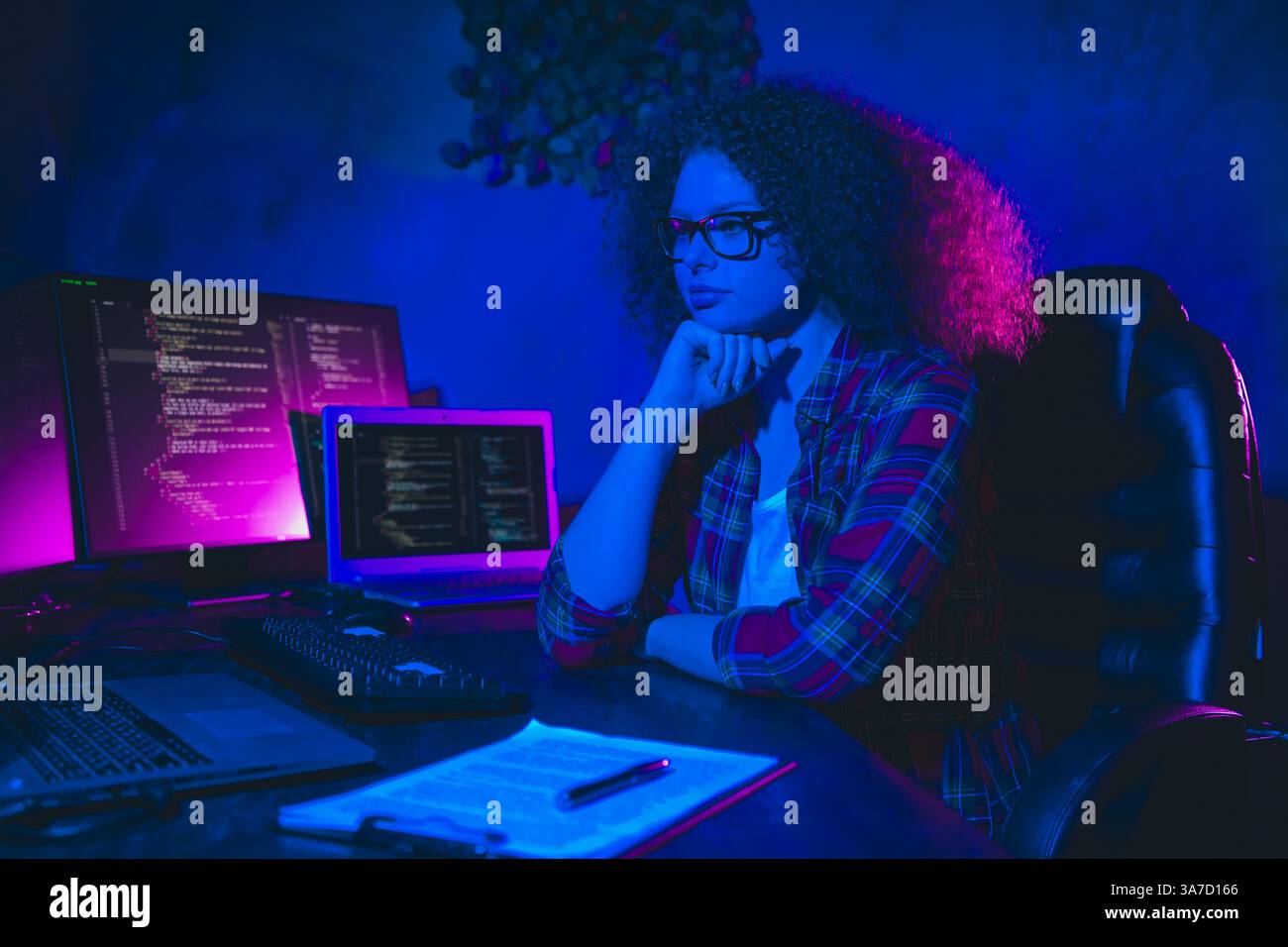 Young female programmer working remotely on her computer in cyberspace, analyzing code within a vibrant and professional home workplace. Stock Photo