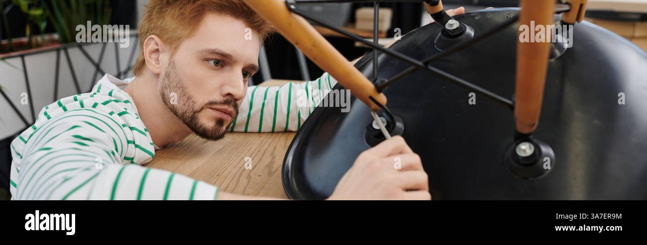 A man carefully assembles a modern chair while unpacking in a new space. Stock Photo