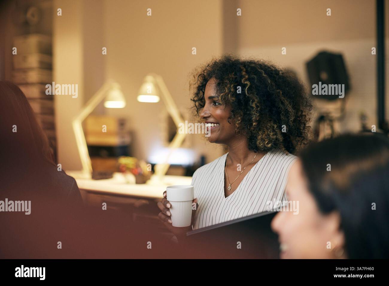 Happy curly haired young businesswoman holding disposable cup at office Stock Photo