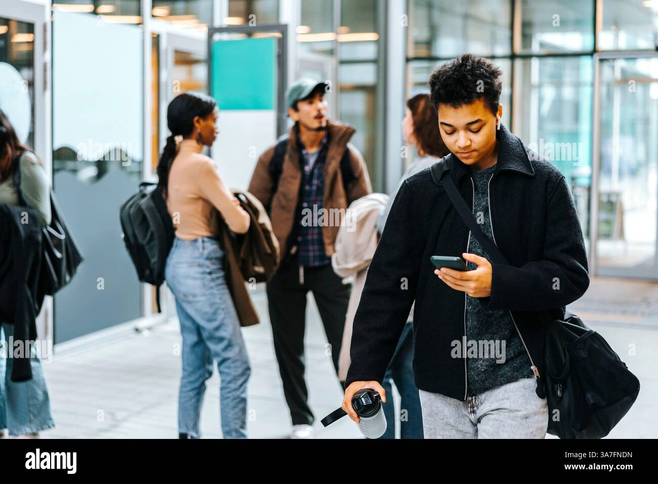 Young man carrying bag using smart phone while walking in tech university campus Stock Photo