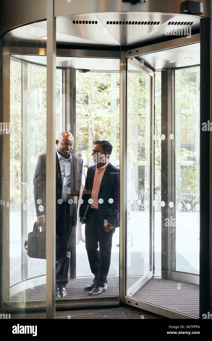 Happy male business colleagues walking through revolving door of office ...