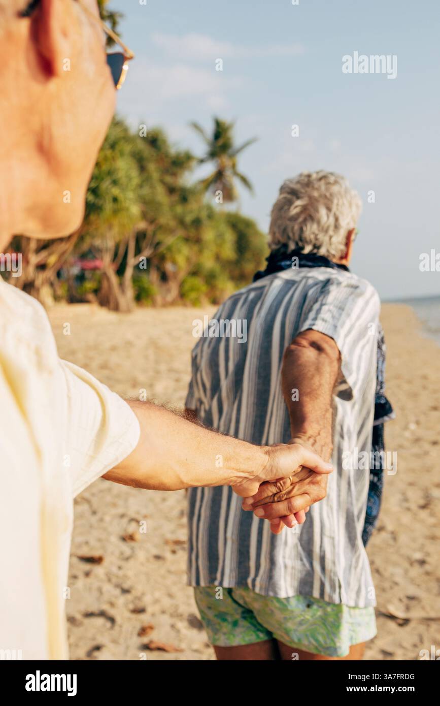 Elderly gay couple holding hands and walking on beach at sunny day Stock Photo