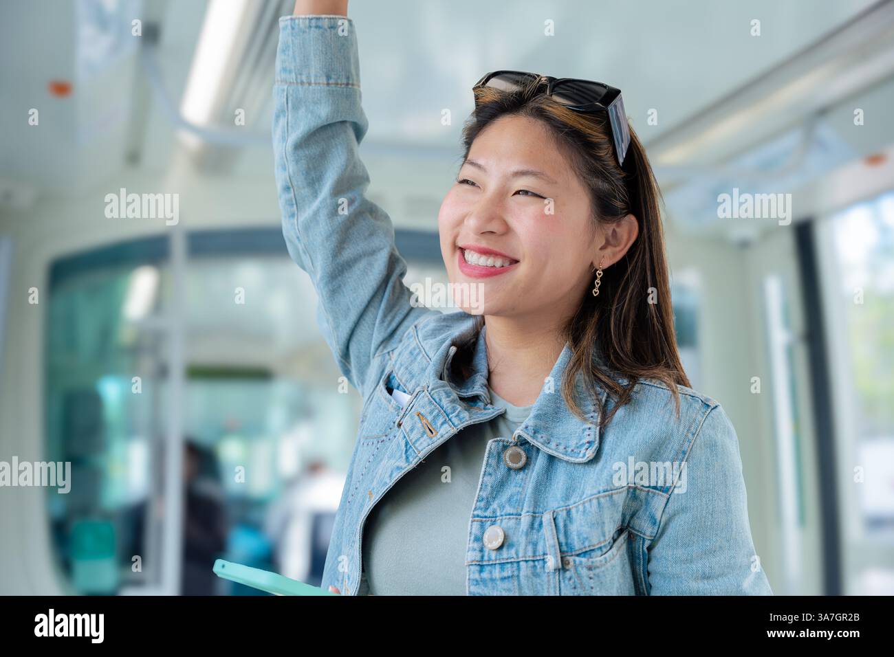 Smiling chinese woman standing on public transport holding handrail and ...
