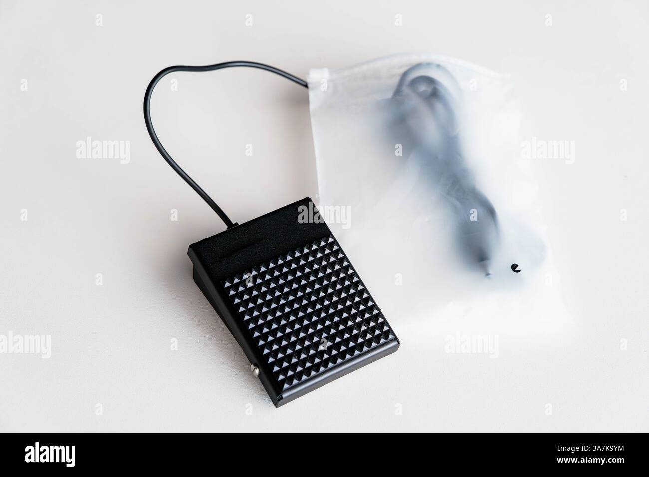 Black Electric Sewing Machine Foot Pedal Controller and Cable in Translucent Plastic Packaging on White Surface. Stock Photo