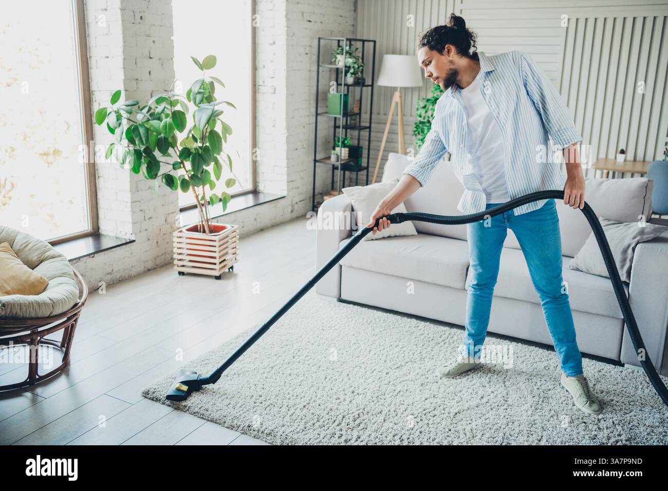 Young man cleaning his modern living room using a vacuum, enjoying a ...
