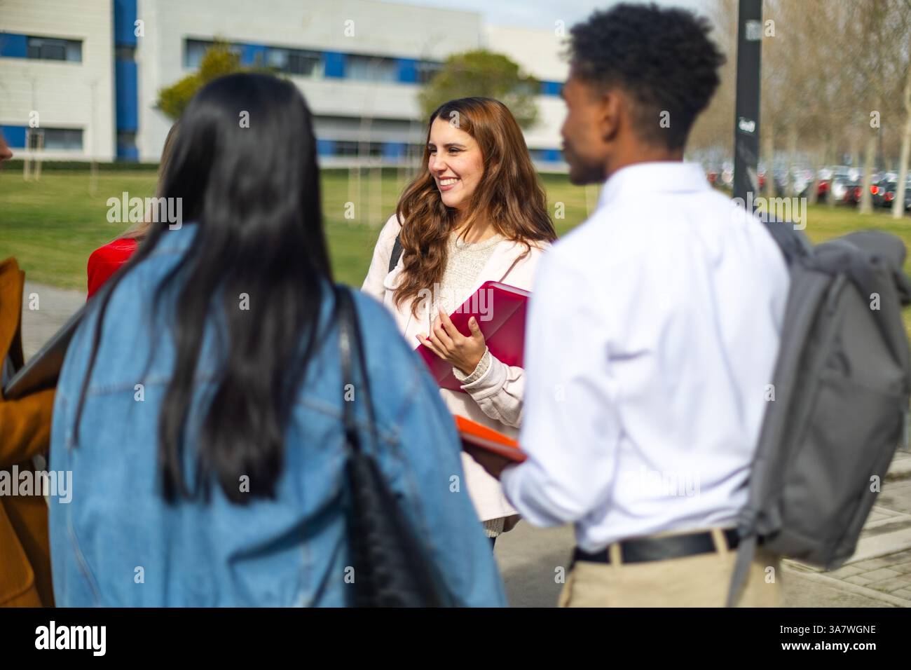 Group of diverse university students walking together on campus, holding notebooks and engaging in conversation Stock Photo