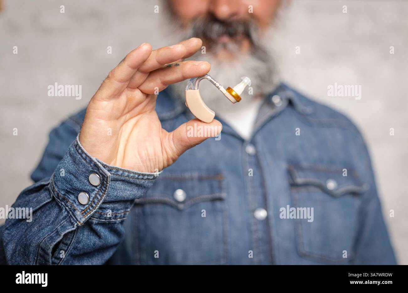 Middle-aged man holding hearing aid in close-up. Treatment of deafness. Stock Photo