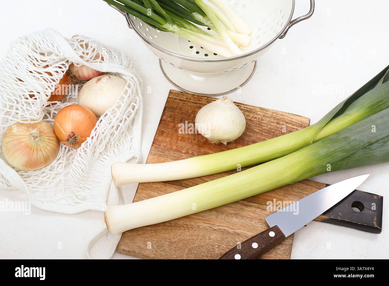 Wooden board and colander with different kinds of onion on white ...
