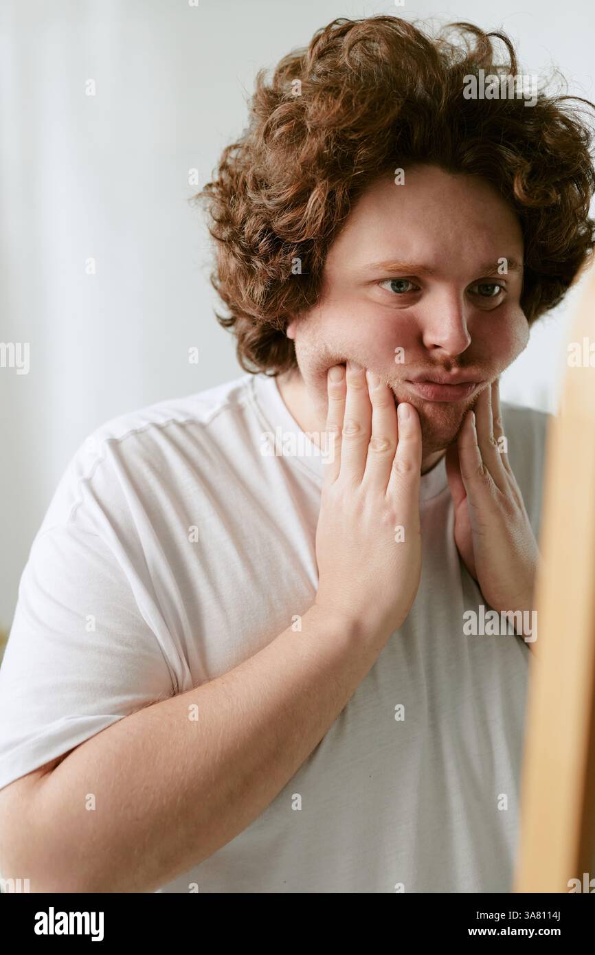 Young Man Wearing White Shirt Touching His Face in Thought Stock Photo