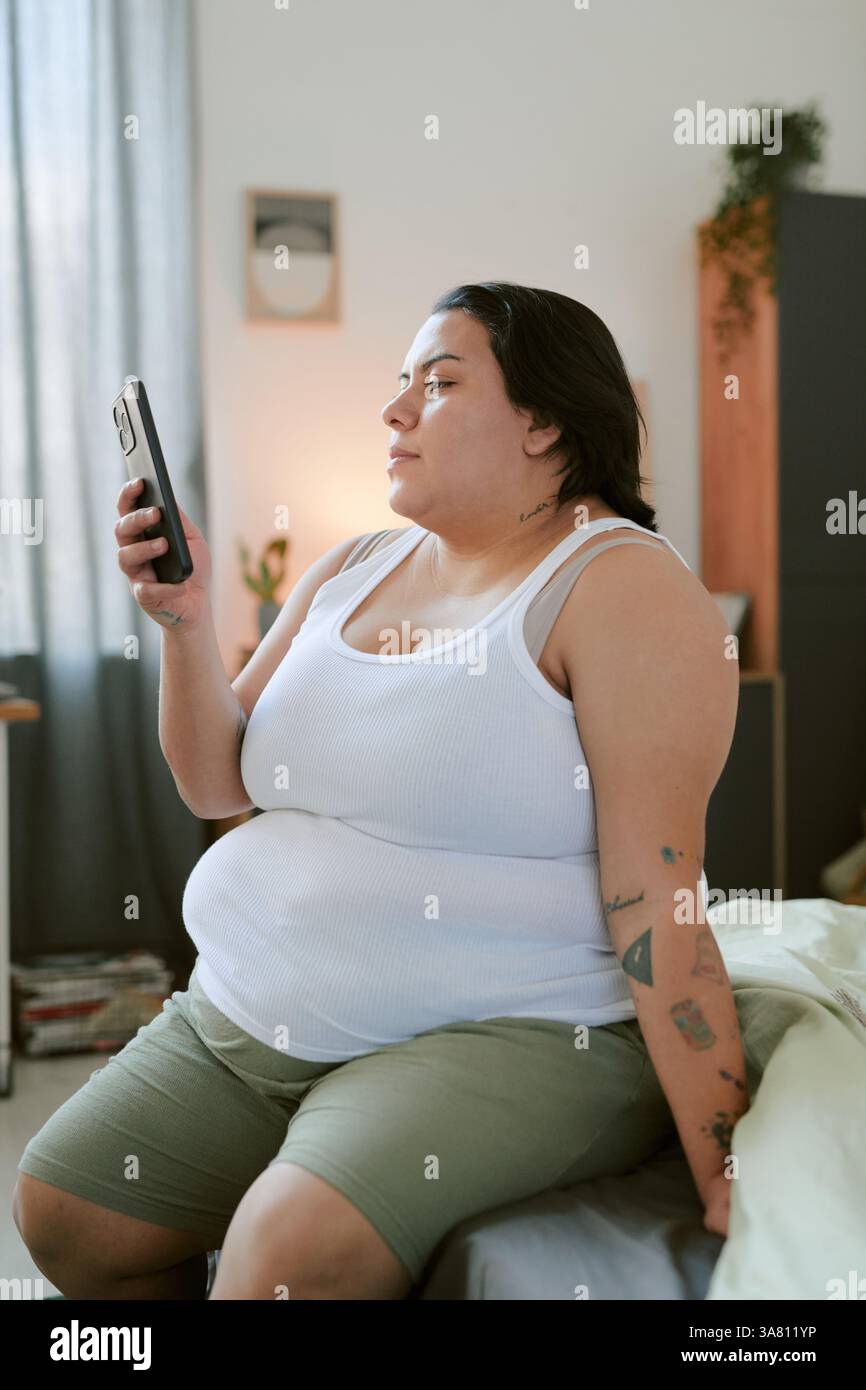 Using Smartphone While Sitting on Bed at Home Stock Photo