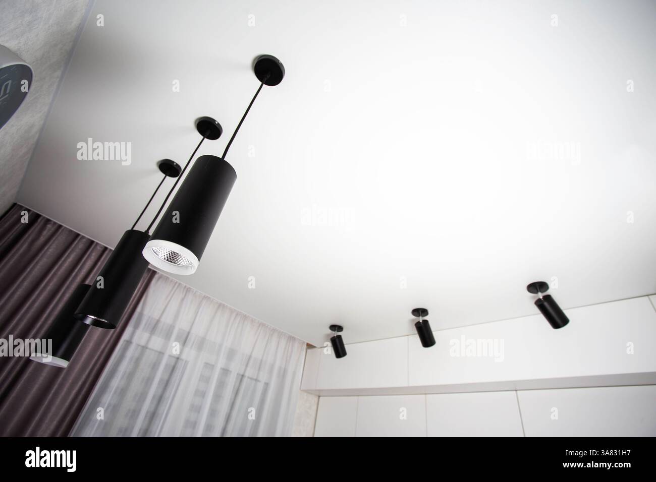 Modern suspended ceiling with different black LED lamps on a white ceiling in the kitchen. Copy space for text Stock Photo