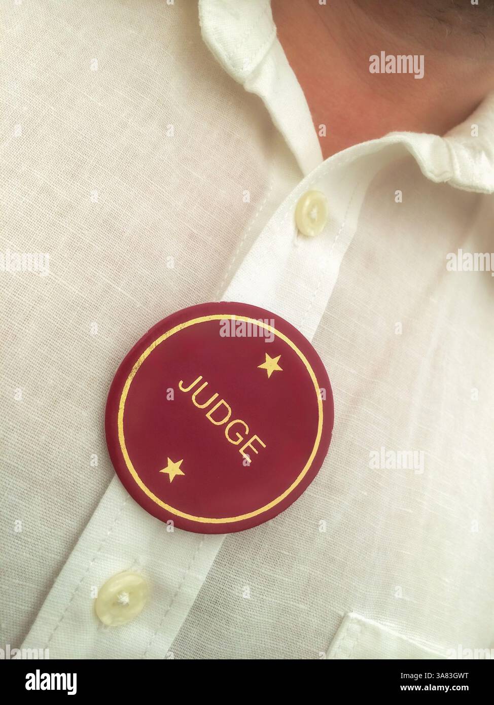 Close-up of a man wearing a white linen shirt with a ‘Judge’ badge pinned to the chest, face not visible Stock Photo