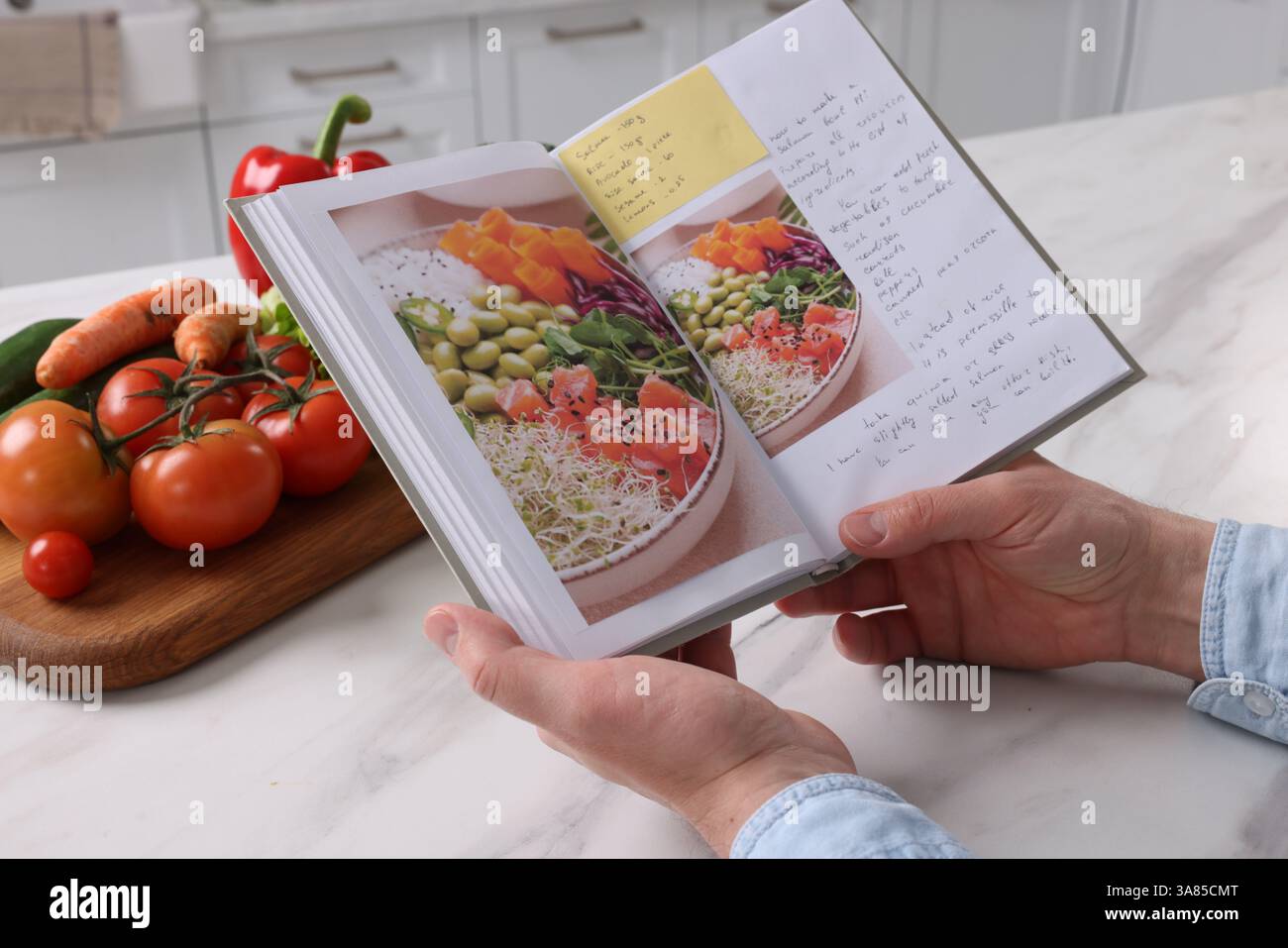 Man with recipe book at white marble table in kitchen, closeup Stock Photo