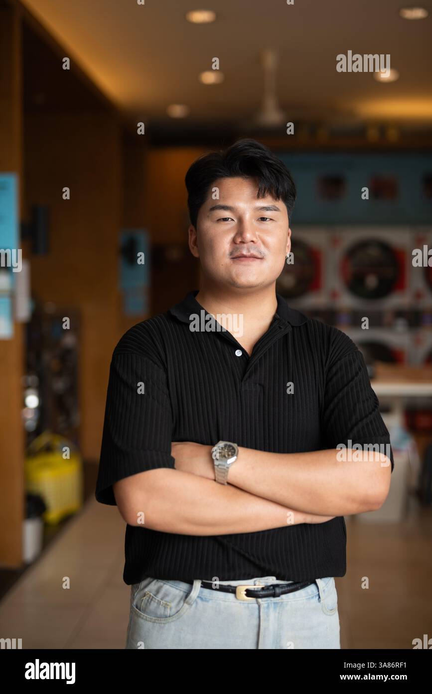 Young Asian man in laundry shop with arms crossed Stock Photo