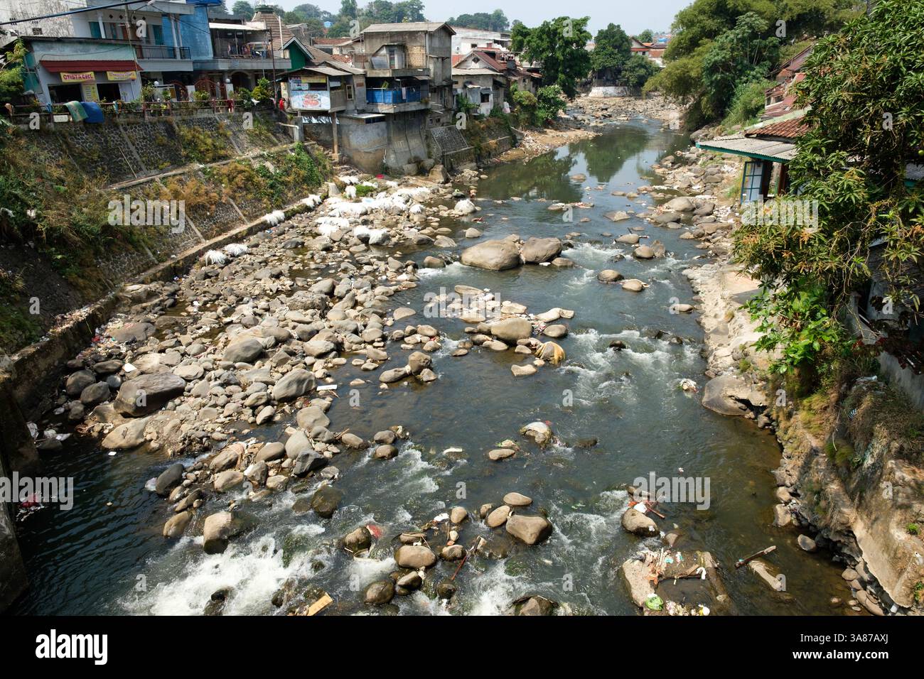 Trash and debris choke a rocky river flowing through a densely ...