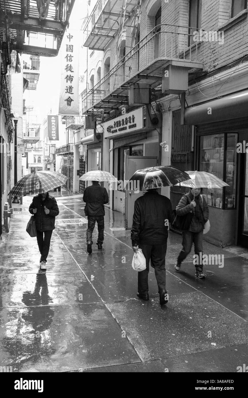 Pedestrians use umbrellas to stay dry while walking down a wet alleyway in Chinatown during a rain shower. Stock Photo