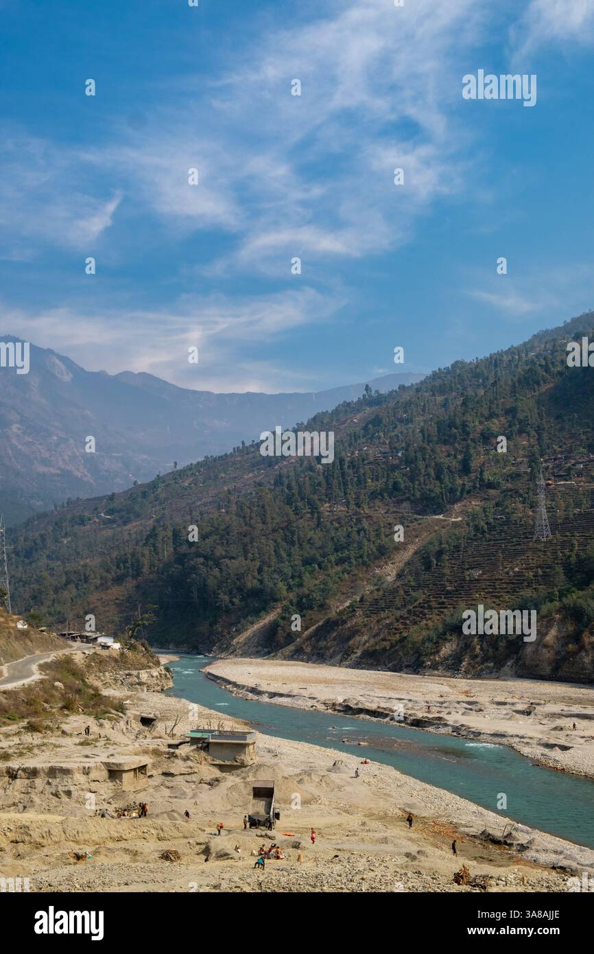 Workers manually extract sand and gravel from a riverbed in a mountain valley, gathering essential construction materials. Stock Photo