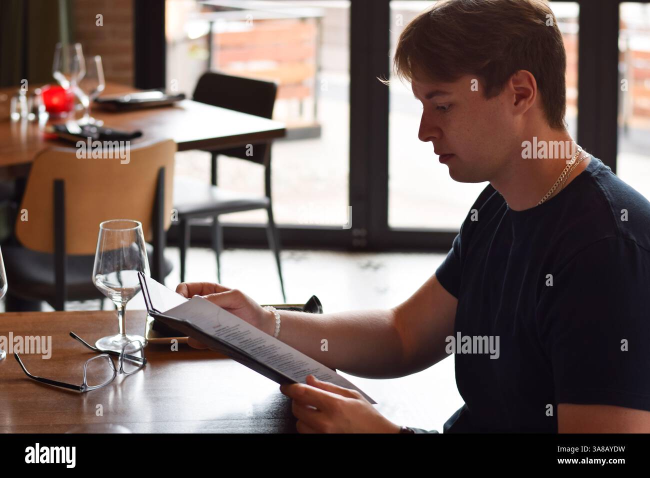 Young man sitting at restaurant table reading menu Stock Photo