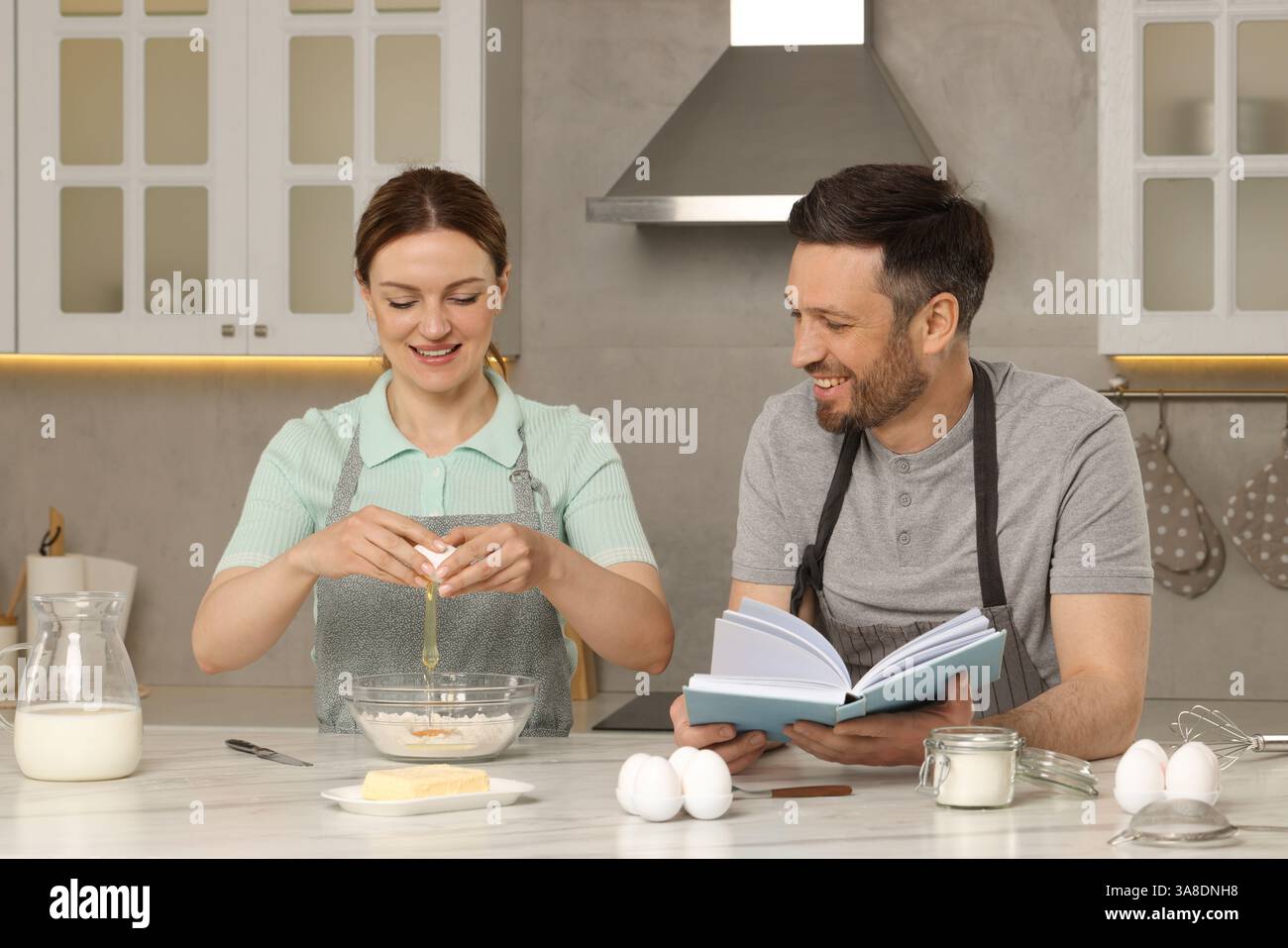 Happy couple cooking by recipe book in kitchen Stock Photo