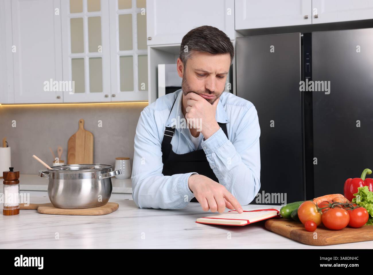 Adult man reading recipe book at white marble table in kitchen Stock Photo