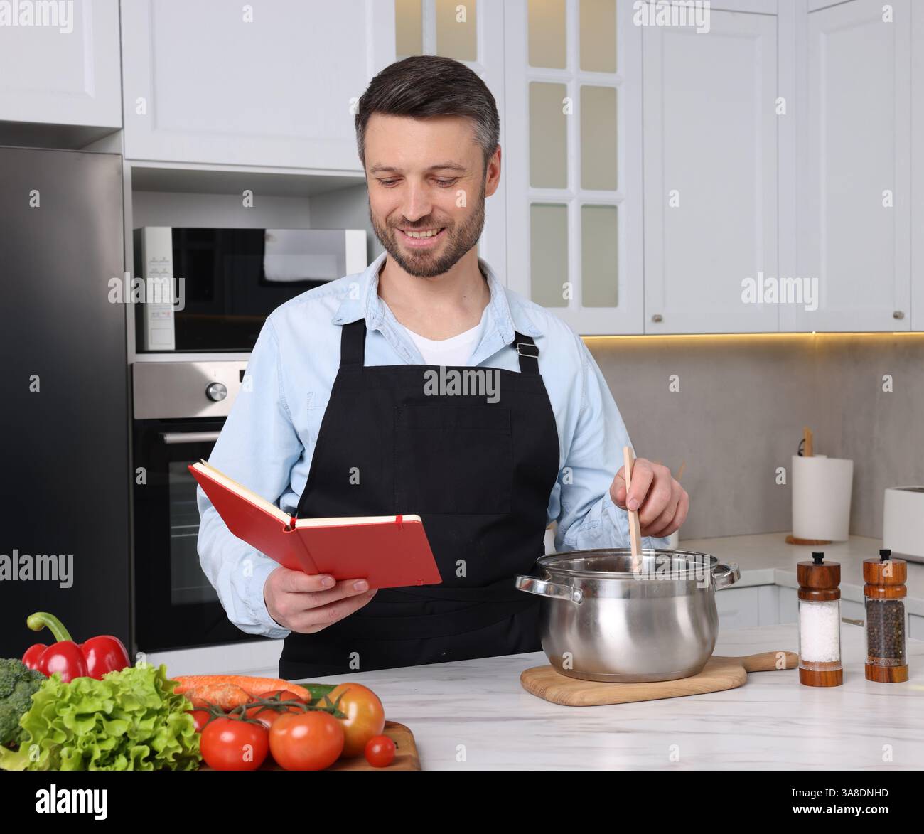 Happy man cooking by recipe book in kitchen Stock Photo