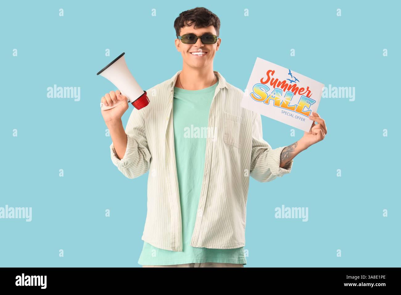 Handsome young man holding paper with text SUMMER SALE and megaphone on blue background Stock Photo