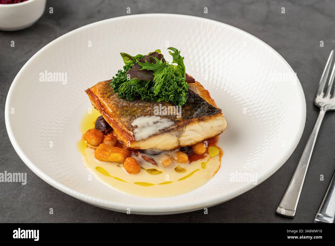 Crispy-skinned pan-seared fish fillet with chickpeas, creamy sauce, and fresh greens Stock Photo