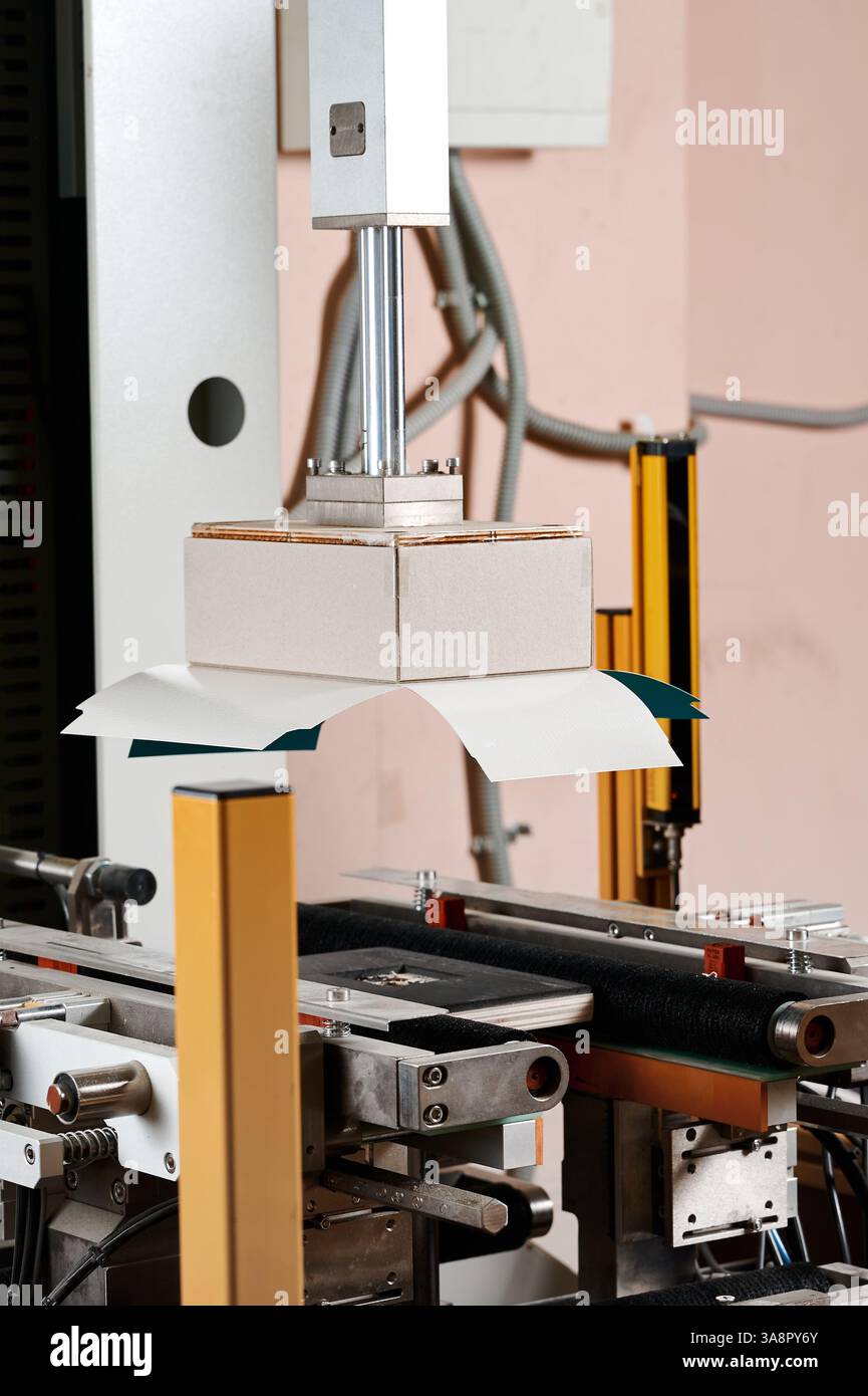 Innovative machine expertly wrapping rectangular boxes in a busy packaging facility during daylight hours Stock Photo