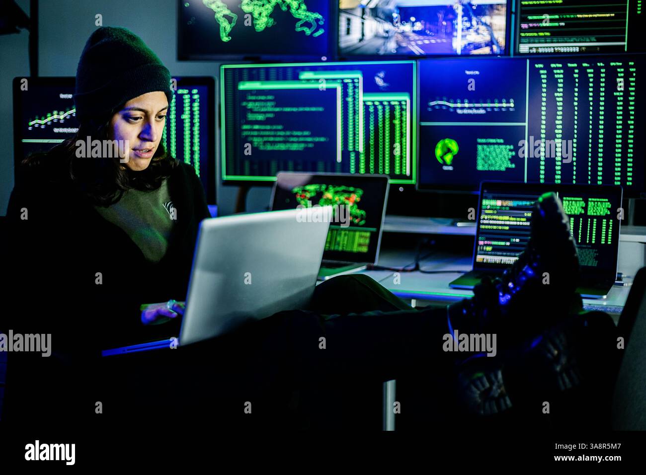 Female hacker breaking into corporate network using laptop and multiple screens Stock Photo