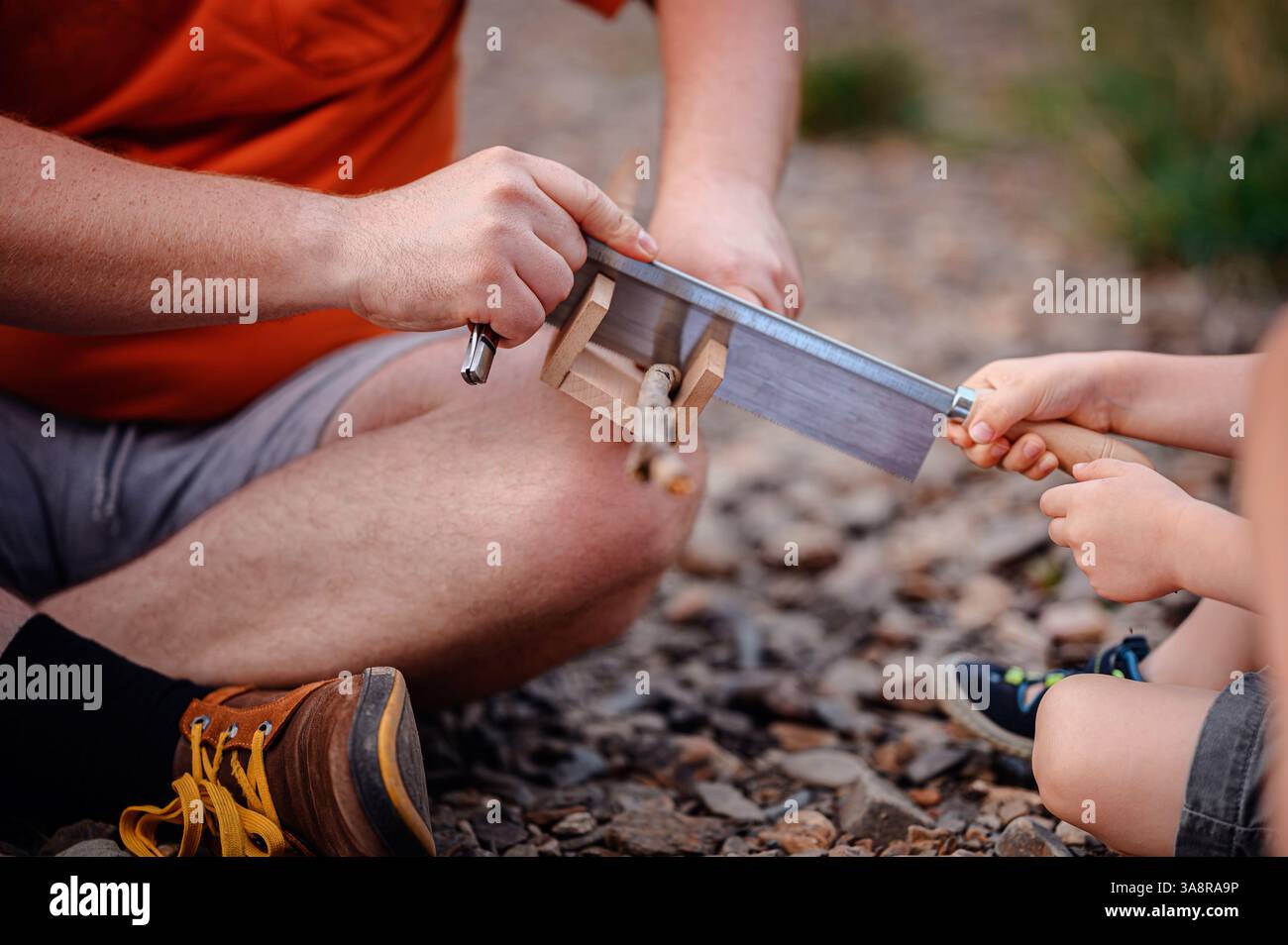 Close-up of a father guiding his child in using a saw to cut a small branch. A hands-on learning experience in nature, emphasizing skill-building and Stock Photo