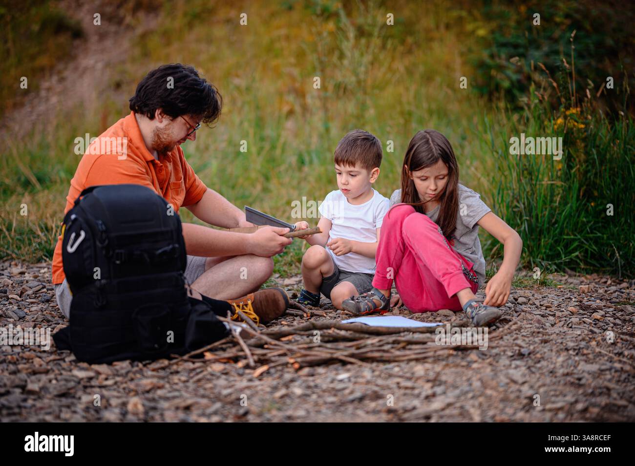 A father teaches his children how to use a saw and gather sticks during an outdoor activity. A hands-on learning experience promoting teamwork, skill- Stock Photo